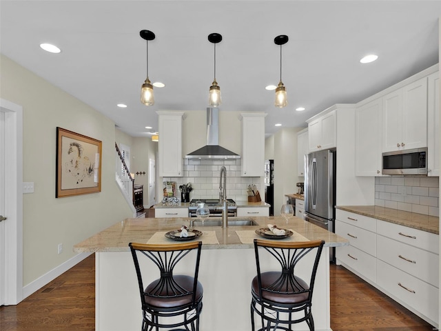 kitchen featuring dark wood-style floors, a breakfast bar area, appliances with stainless steel finishes, white cabinets, and wall chimney range hood