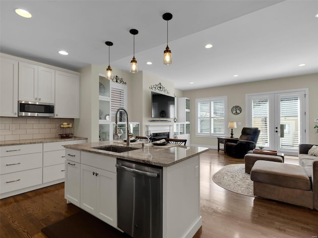 kitchen with a sink, open floor plan, appliances with stainless steel finishes, light stone countertops, and dark wood finished floors