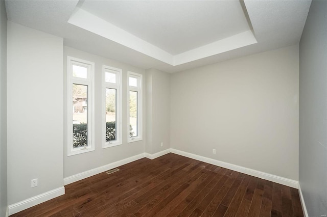 spare room featuring dark wood finished floors, visible vents, a raised ceiling, and baseboards