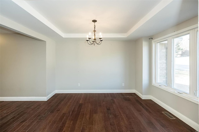 empty room featuring a tray ceiling, dark wood-style floors, and baseboards