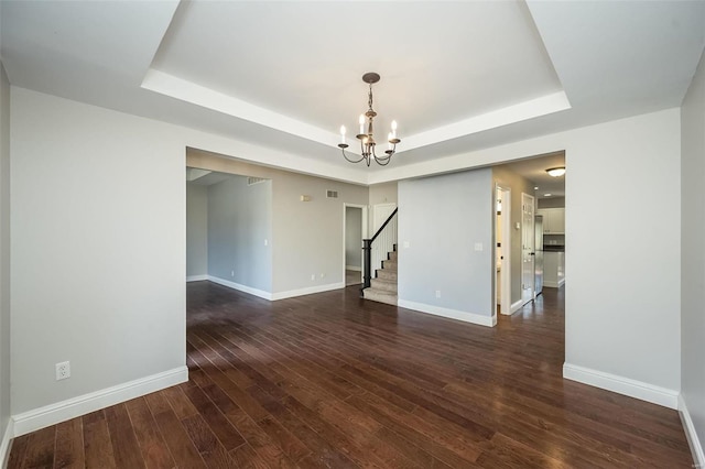 unfurnished room with a tray ceiling, baseboards, dark wood-type flooring, and stairway