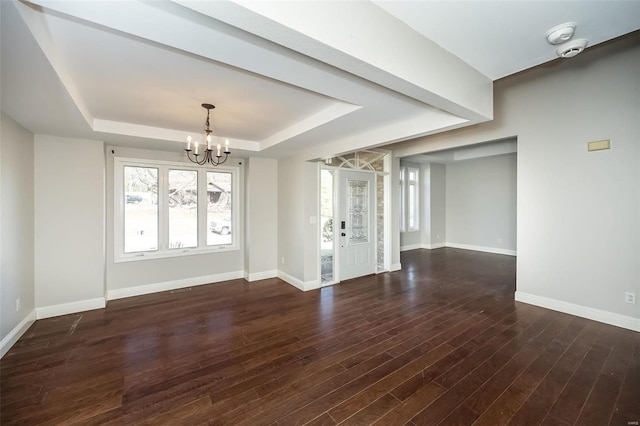 spare room featuring a tray ceiling, baseboards, wood finished floors, and a chandelier