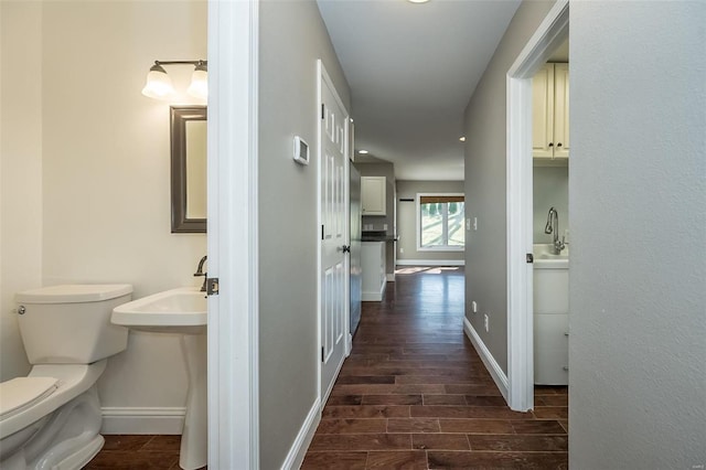 hallway with baseboards, wood finish floors, and a sink