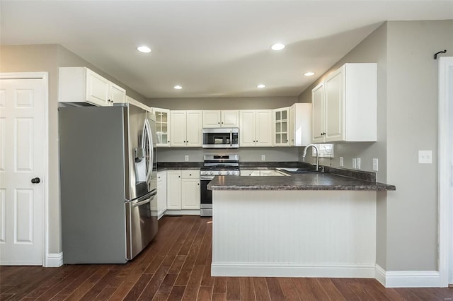 kitchen featuring dark wood-style floors, a peninsula, a sink, stainless steel appliances, and glass insert cabinets