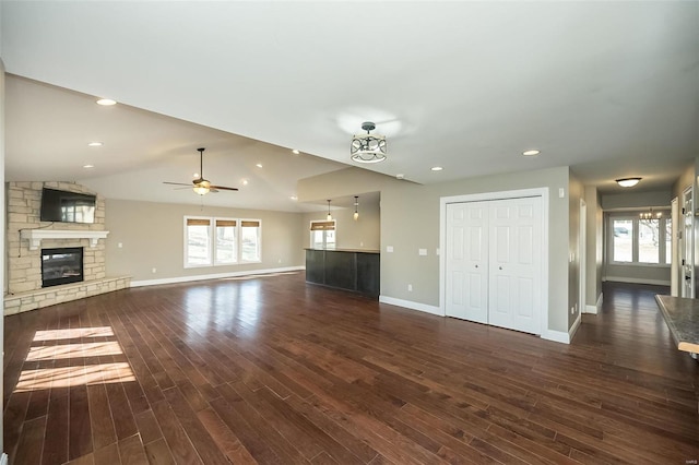 unfurnished living room with a stone fireplace, plenty of natural light, dark wood-type flooring, and vaulted ceiling