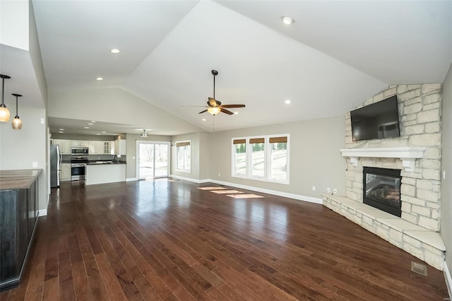 unfurnished living room with a stone fireplace, vaulted ceiling, a ceiling fan, and dark wood-style flooring