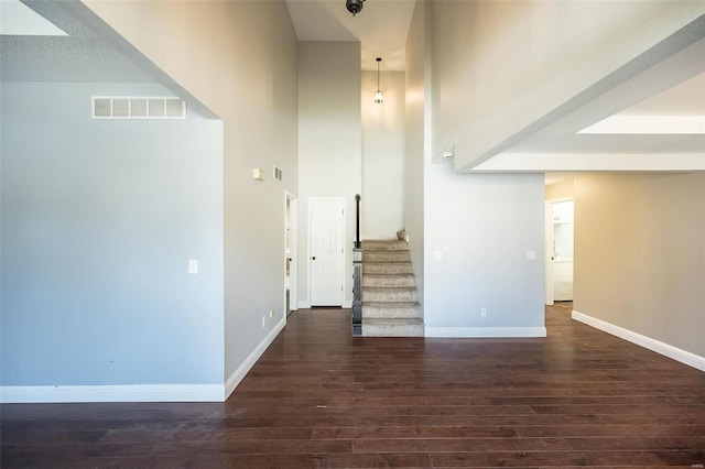 interior space with visible vents, baseboards, wood finished floors, and a towering ceiling