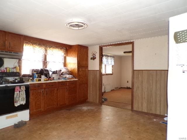 kitchen featuring wainscoting, brown cabinets, wood walls, and electric range