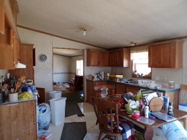 kitchen with brown cabinets, lofted ceiling, ornamental molding, a sink, and a textured ceiling