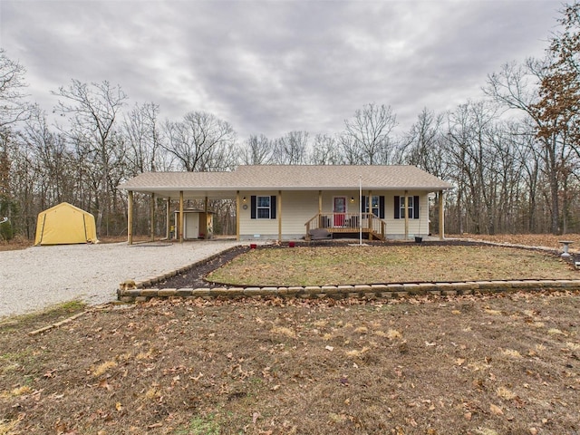 ranch-style home featuring an outbuilding, gravel driveway, a porch, a shed, and a carport