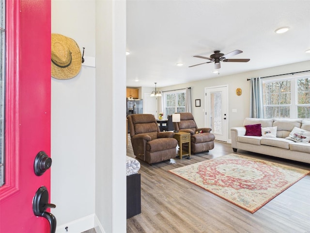 living room featuring ceiling fan with notable chandelier, recessed lighting, wood finished floors, and baseboards