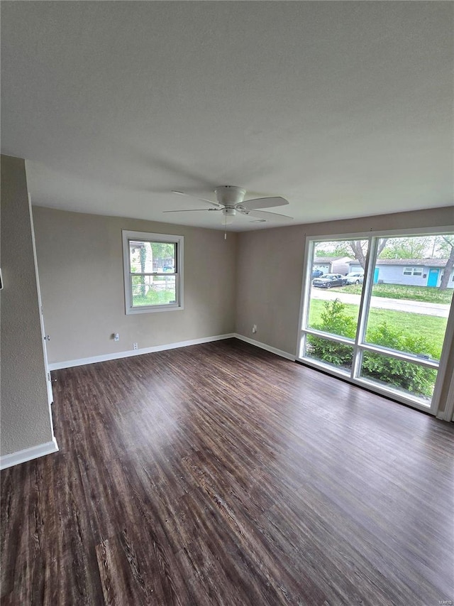 empty room with a ceiling fan, baseboards, and dark wood finished floors