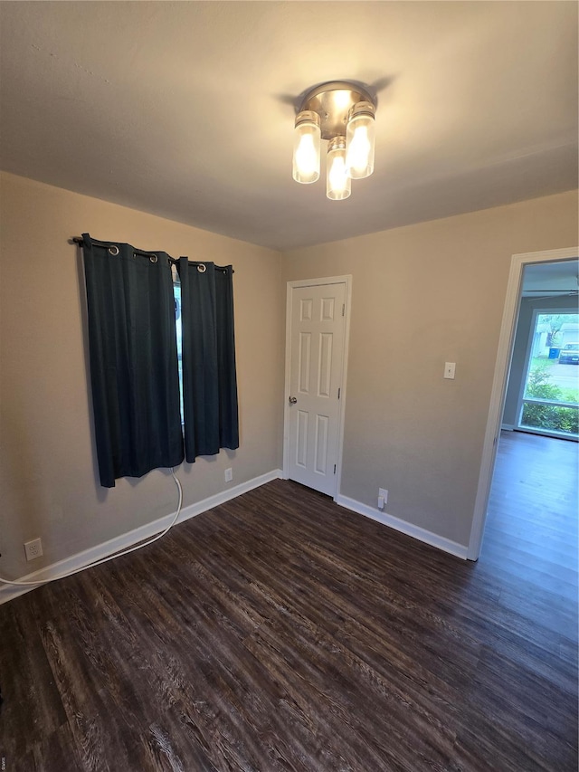 spare room with baseboards, dark wood-style flooring, and a chandelier