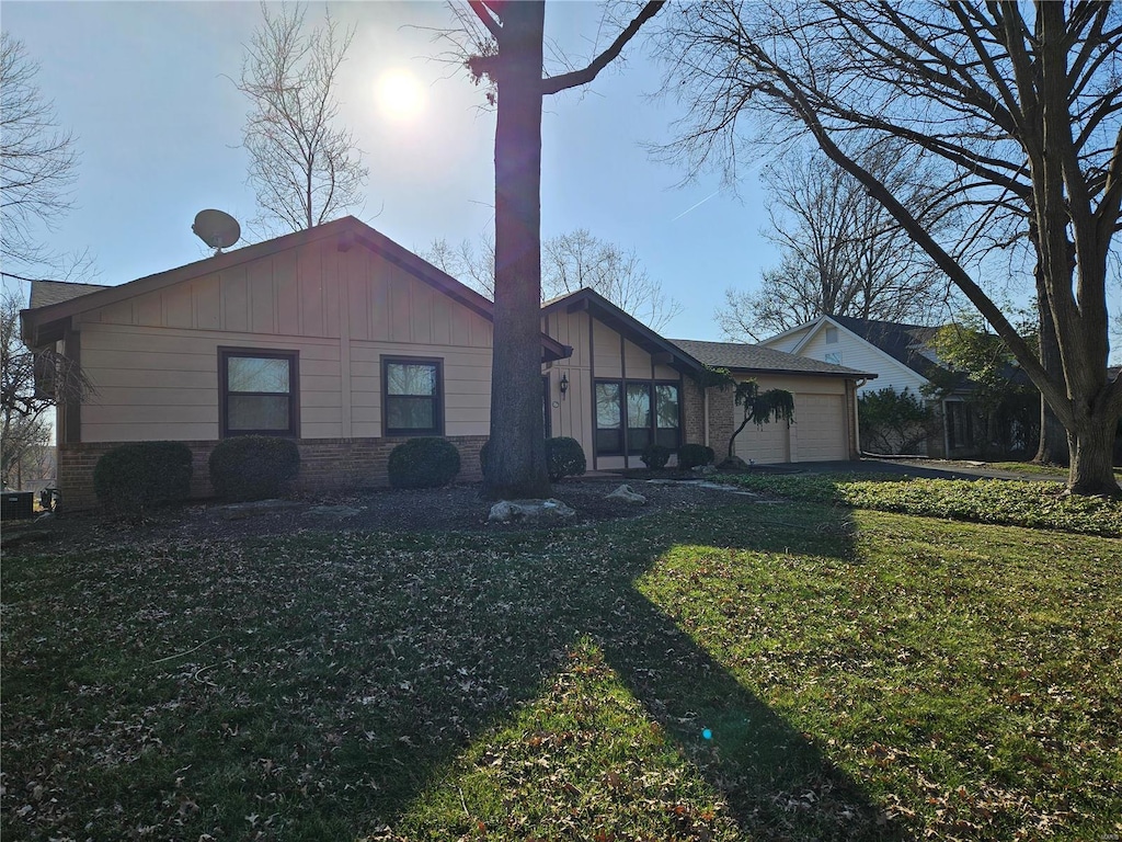 view of front of house with brick siding, a garage, board and batten siding, and a front yard