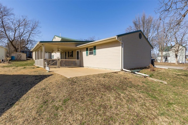 rear view of property featuring a lawn, a ceiling fan, an outdoor structure, a patio area, and a shed