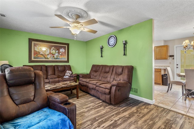 living area with light wood finished floors, visible vents, a textured ceiling, and ceiling fan with notable chandelier