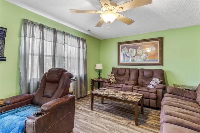 living room featuring ceiling fan, a textured ceiling, wood finished floors, and visible vents