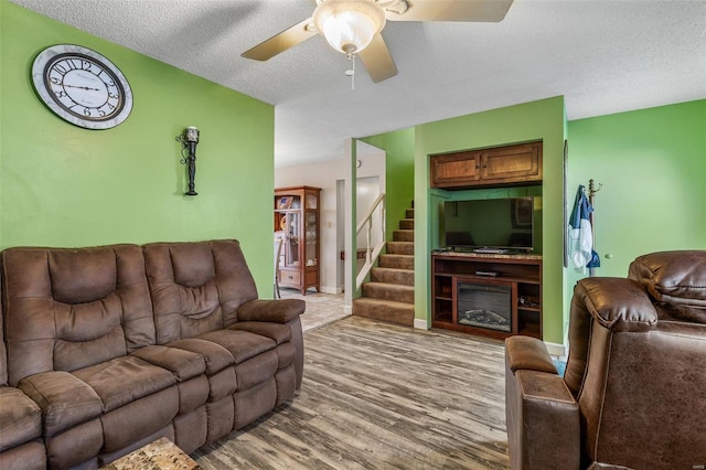 living room featuring baseboards, a ceiling fan, wood finished floors, stairs, and a textured ceiling