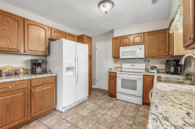 kitchen with white appliances, brown cabinets, a sink, and light tile patterned floors