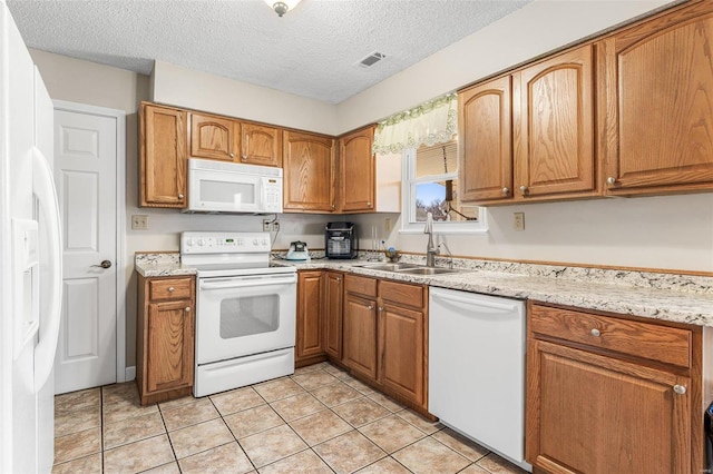 kitchen featuring brown cabinets, light tile patterned floors, visible vents, a sink, and white appliances