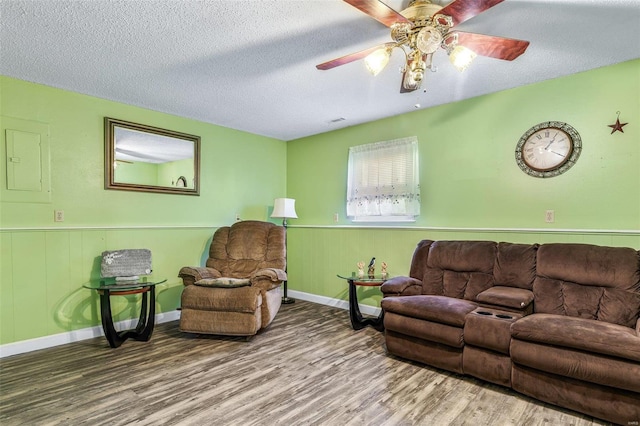 living room featuring a textured ceiling, ceiling fan, wainscoting, and wood finished floors