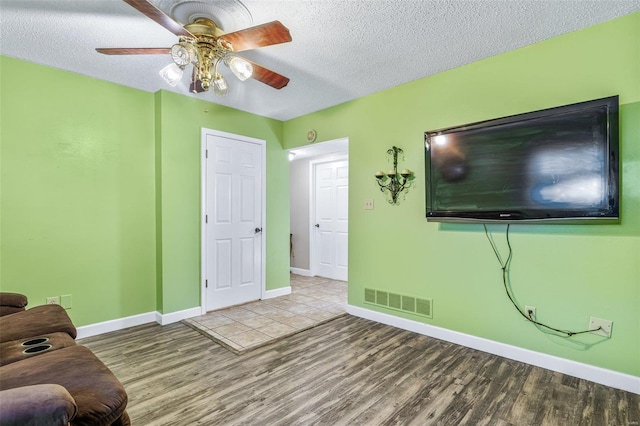 living room featuring baseboards, visible vents, a ceiling fan, wood finished floors, and a textured ceiling