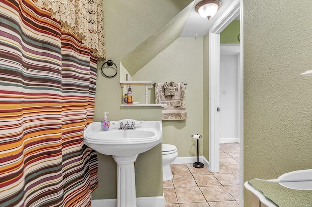 bathroom with a textured wall, curtained shower, toilet, baseboards, and tile patterned floors