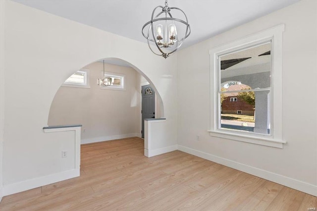 unfurnished dining area featuring baseboards, arched walkways, a notable chandelier, and wood finished floors