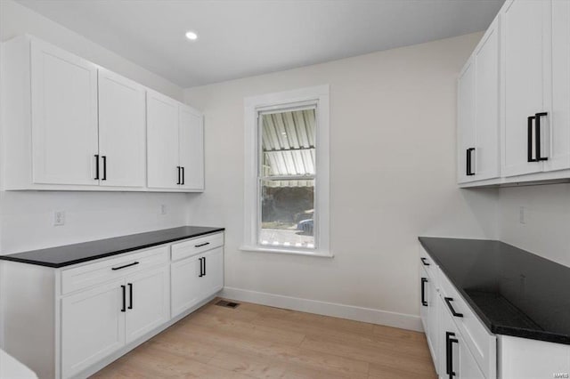 kitchen featuring dark countertops, white cabinets, light wood finished floors, and baseboards