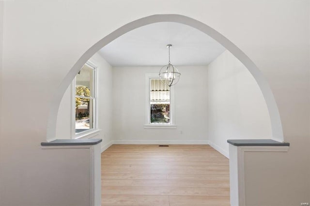 unfurnished dining area with light wood-type flooring, visible vents, baseboards, and a chandelier