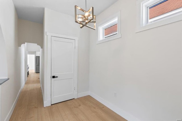 corridor featuring light wood finished floors, baseboards, and an inviting chandelier