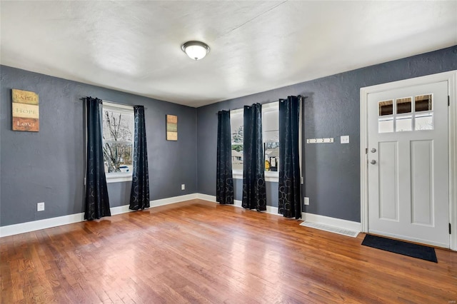 foyer entrance with a textured wall, baseboards, and wood-type flooring