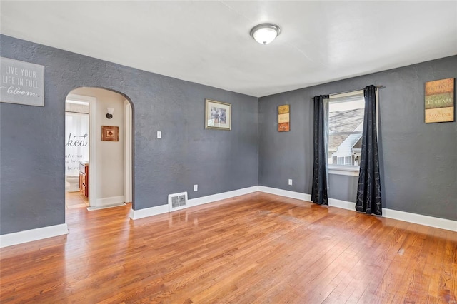 unfurnished room featuring visible vents, baseboards, a textured wall, arched walkways, and wood-type flooring