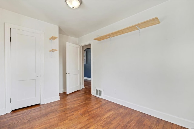 spare room featuring visible vents, baseboards, arched walkways, and wood finished floors