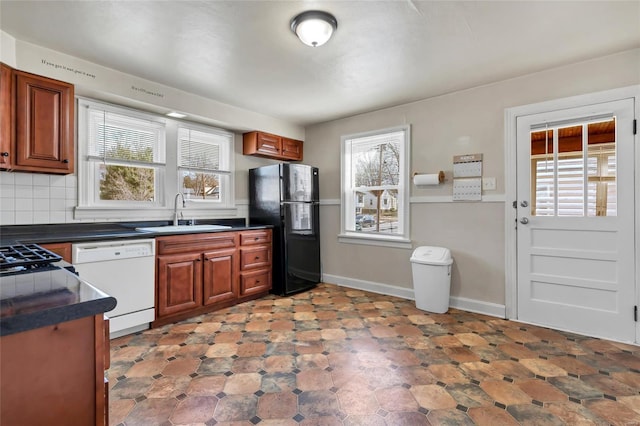 kitchen with white dishwasher, freestanding refrigerator, a sink, dark countertops, and tasteful backsplash