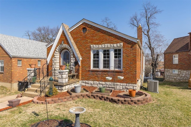 english style home with a chimney, brick siding, central AC, and a front yard