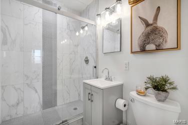 bathroom featuring a marble finish shower, toilet, and vanity