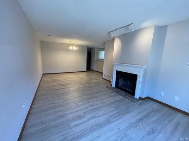 unfurnished living room featuring rail lighting, a fireplace with flush hearth, wood finished floors, and baseboards