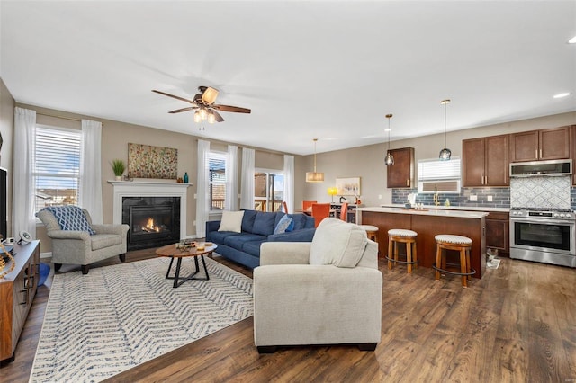 living area featuring a glass covered fireplace, dark wood-style flooring, and ceiling fan