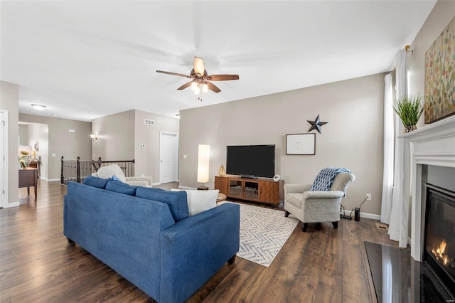 living area with a glass covered fireplace, visible vents, dark wood finished floors, and baseboards