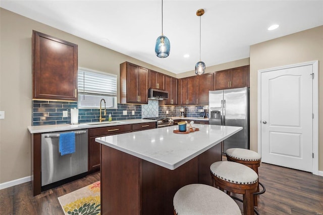 kitchen with a breakfast bar, a center island, backsplash, appliances with stainless steel finishes, and a sink