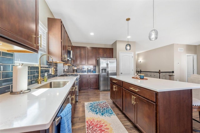 kitchen with a kitchen island, a sink, appliances with stainless steel finishes, decorative backsplash, and dark wood finished floors