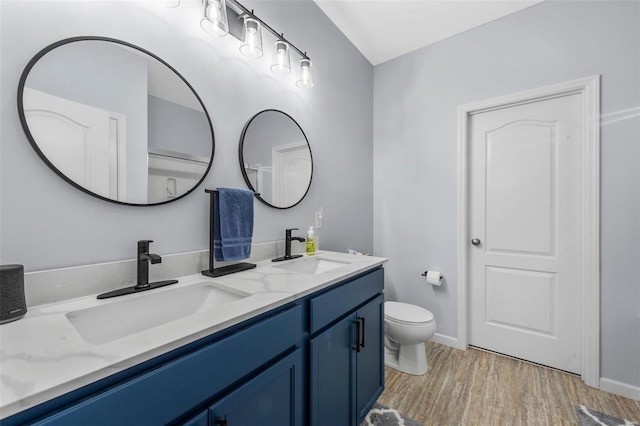 bathroom with double vanity, a sink, toilet, and wood finished floors