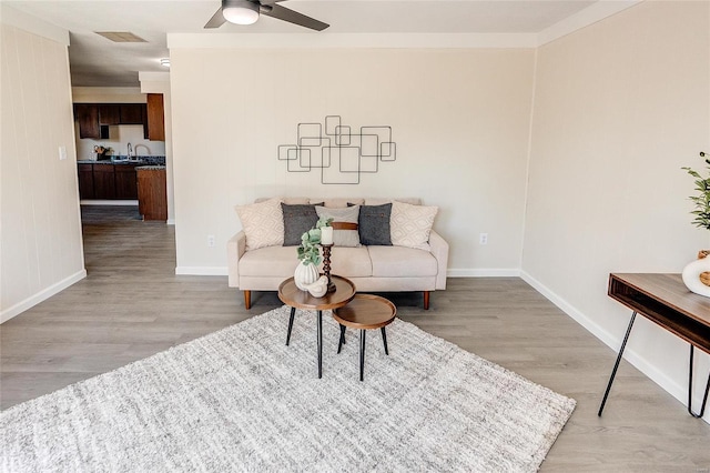 living area featuring light wood-type flooring, baseboards, visible vents, and a ceiling fan