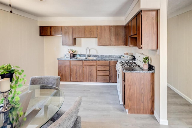 kitchen featuring a sink, light wood-style floors, white range with gas cooktop, and dark countertops