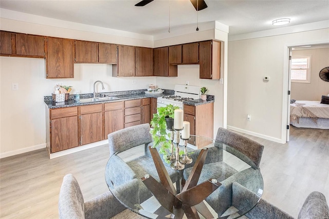 kitchen with dark countertops, ceiling fan, white gas stove, light wood-style flooring, and a sink