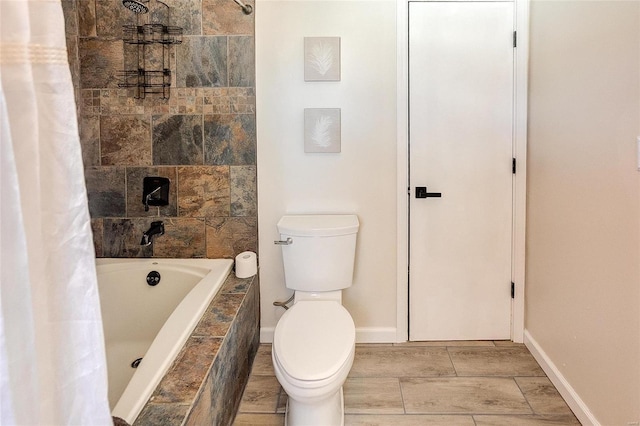 bathroom featuring toilet, baseboards, and tiled shower / bath combo