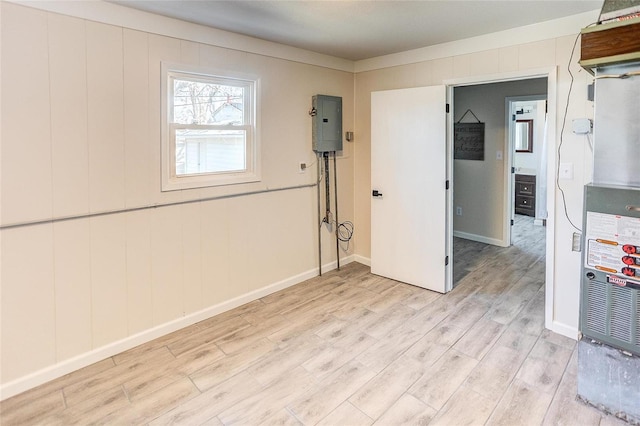 spare room with electric panel, baseboards, and light wood-style floors