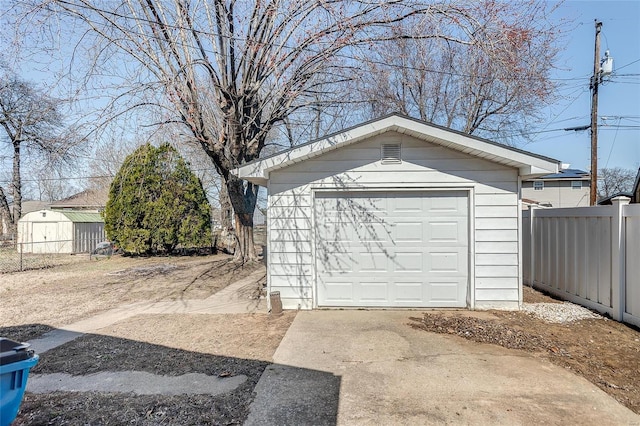 detached garage featuring concrete driveway and fence