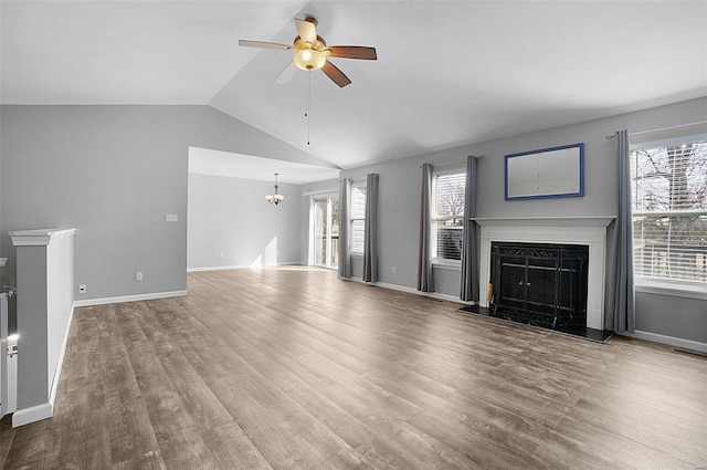 unfurnished living room with wood finished floors, baseboards, lofted ceiling, a fireplace, and ceiling fan with notable chandelier